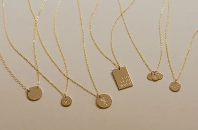 Multiple gold pendant necklace with different shapes and sizes of engraved charms.