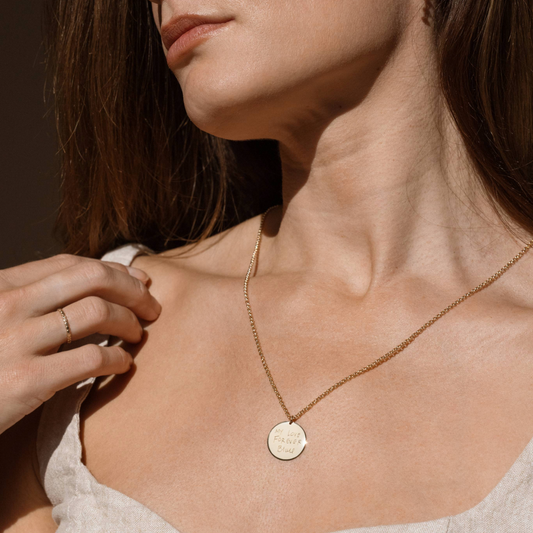 A model wearing a 3/4-inch gold circle necklace on a rolo chain, engraved with handwriting.