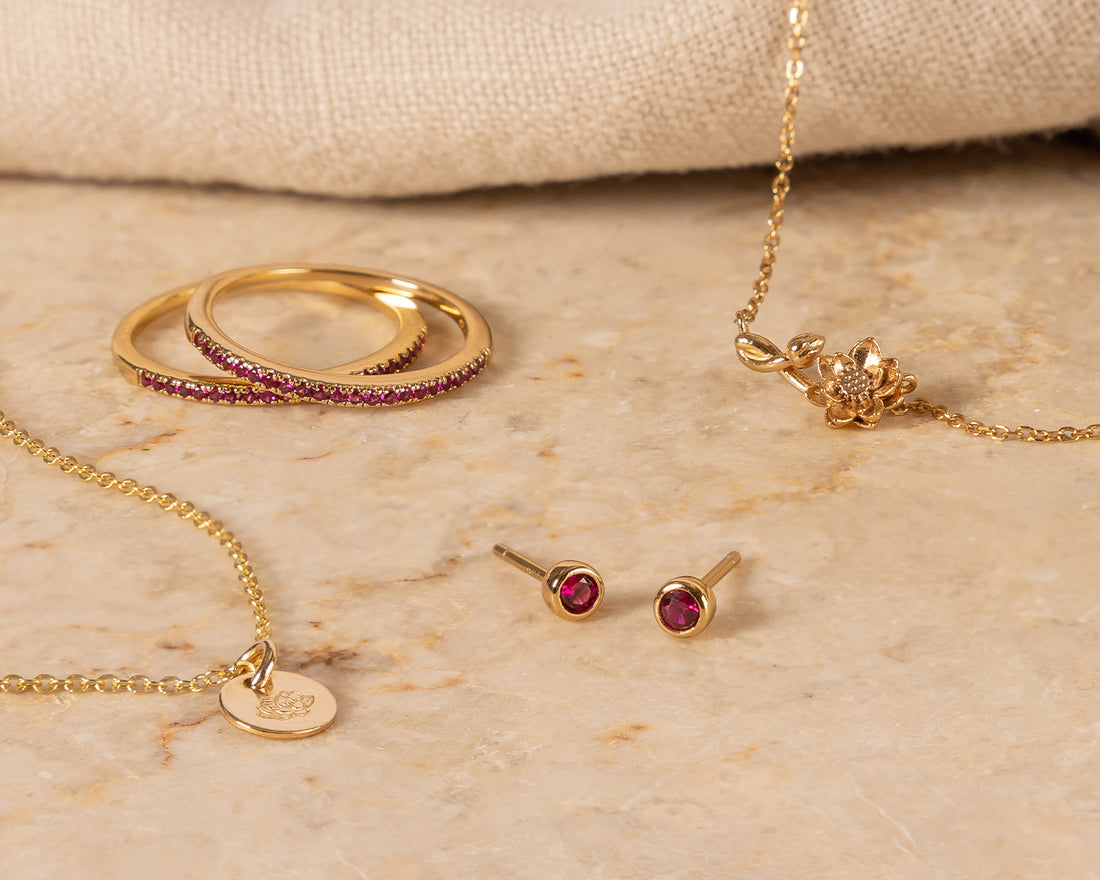 Multiple pieces of gold jewelry representing July with dark red gemstones and lotus flowers.