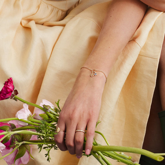 A woman wearing a gold charm bracelet with a small flower charm and light blue gemstone charm.