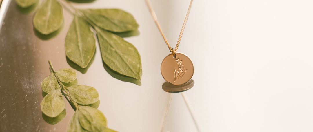 A gold round disc pendant necklace with a lily of the valley engraving.