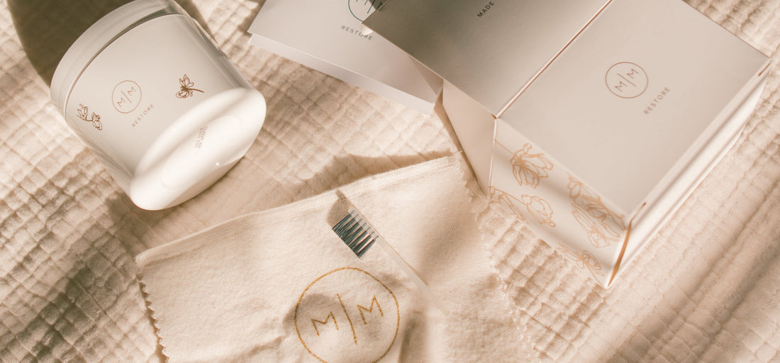 A white jar of jewelry cleaner, a polishing cloth, and a brush laying on a linen surface.