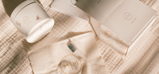A white jar of jewelry cleaner, a polishing cloth, and a brush laying on a linen surface.