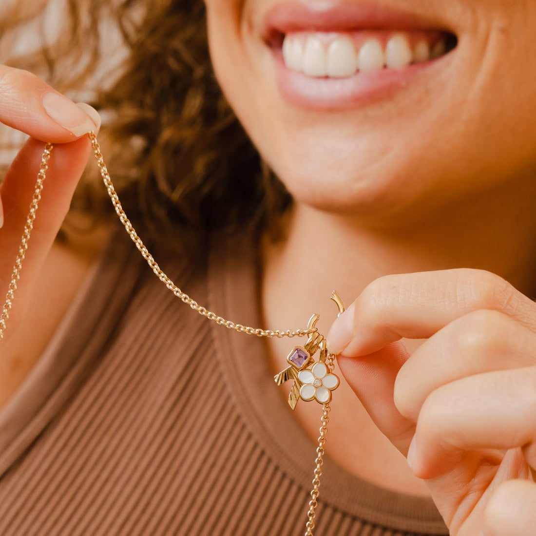 A woman holding a gold rolo charm necklace with an open link lock, showing how to add charms.