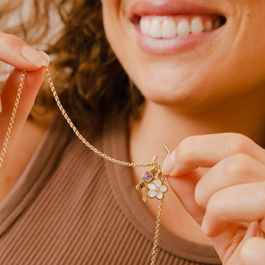 A woman holding a gold rolo charm necklace with an open link lock, showing how to add charms.