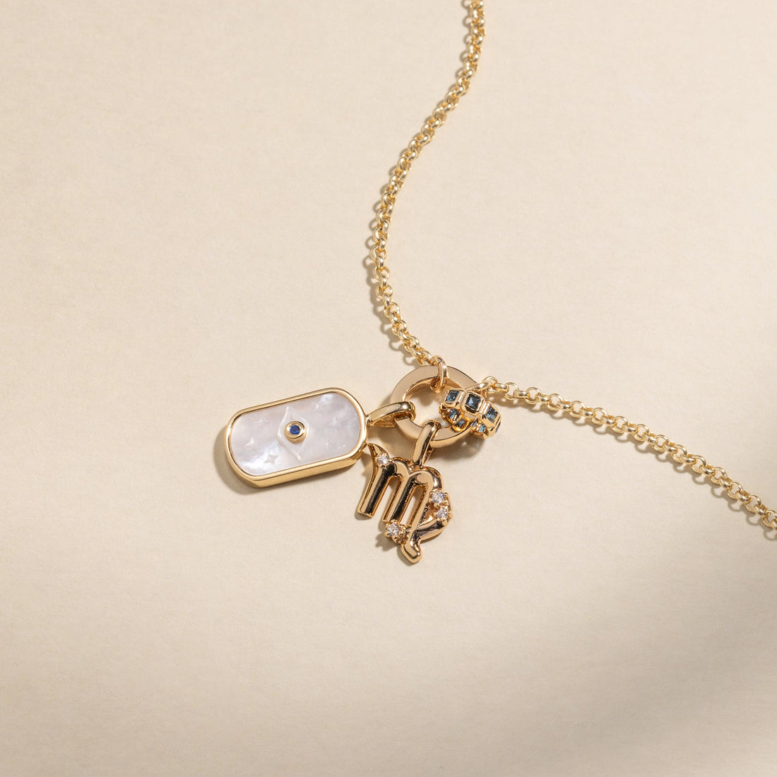 A gold charm necklace with an evil eye charm, a zodiac symbol charm, and a round ring charm with small colored gemstones.