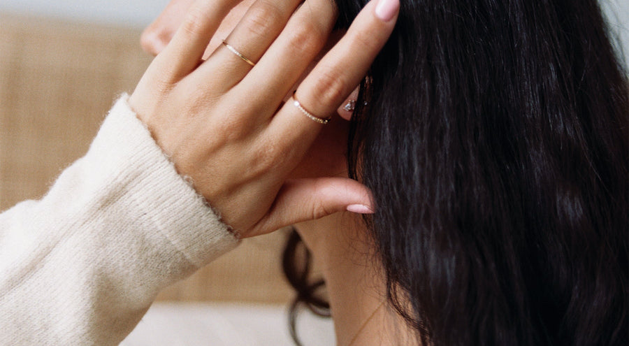 A person's hand on their head, wearing two dainty gold rings with diamonds.