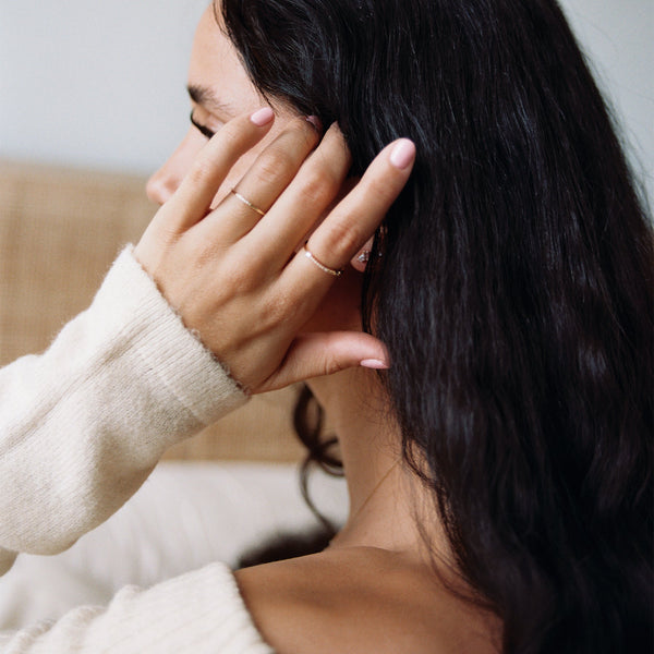 A person's hand on their head, wearing two dainty gold rings with diamonds.