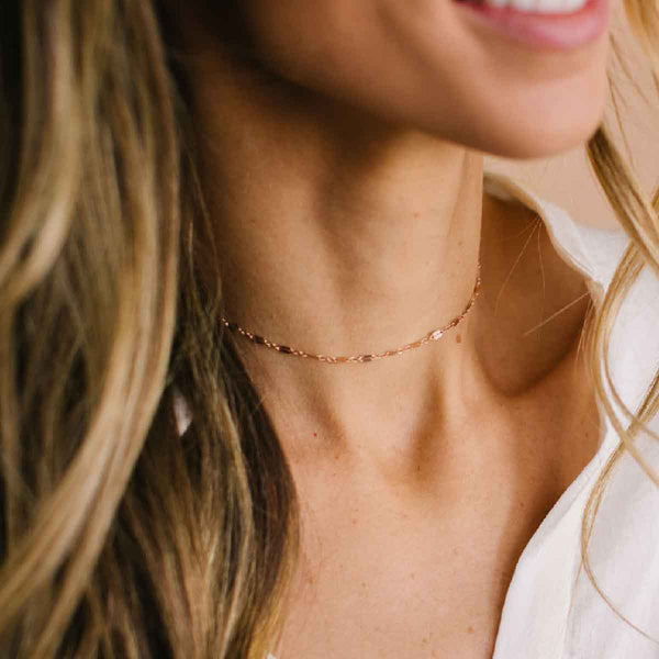 A woman wearing a delicate textured rose gold chain choker.