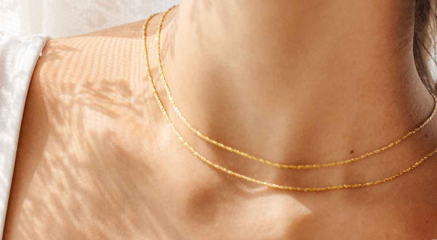 A model wearing two delicate gold chain necklaces.
