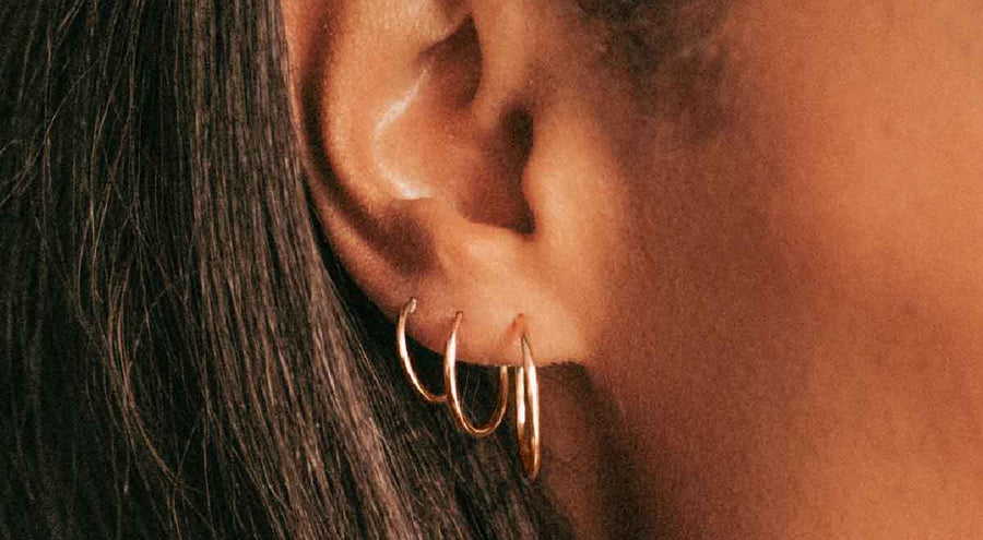 A close-up of a person's ear wearing multiple sizes of thin gold wire hoop earrings.
