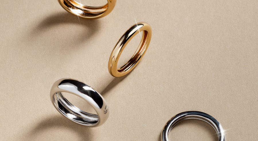 Two gold and two silver polished bold rings, scattered on a light grey surface.