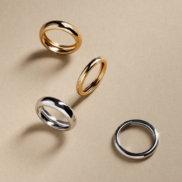 Two gold and two silver polished bold rings, scattered on a light grey surface.