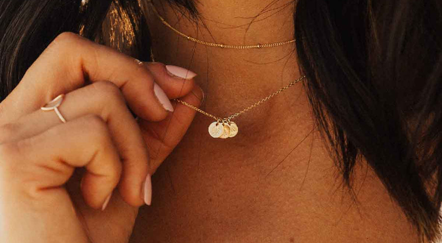 A model wearing a delicate gold pendant chain with multiple engraved round disc charms.