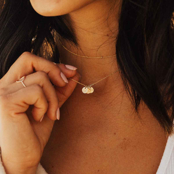A model wearing a delicate gold pendant chain with multiple engraved round disc charms.