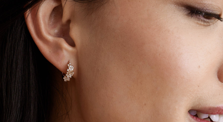 A woman wearing a gold hoop earring with flowers made up of clear gemstones.