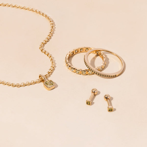 A gold necklace, rings, and earrings all adorned with light green gemstones.
