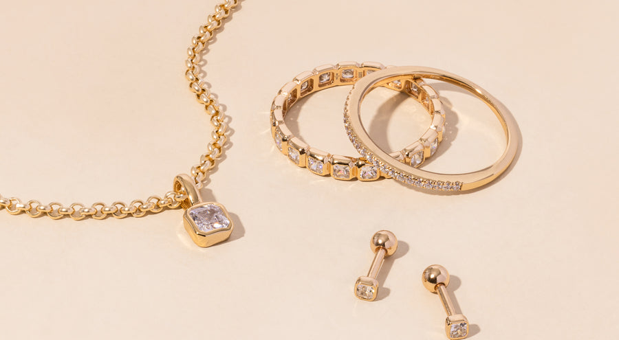 A gold necklace, rings, and earrings all adorned with clear gemstones.
