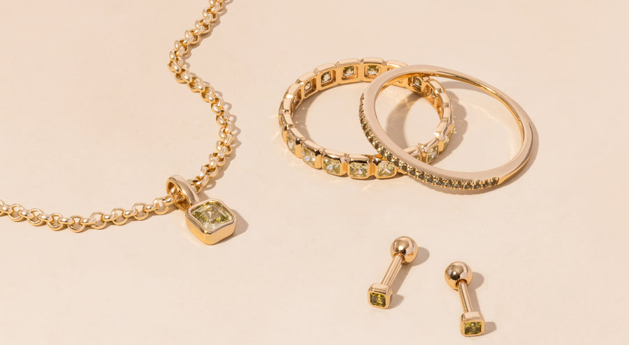 A gold necklace, rings, and earrings all adorned with light green gemstones.