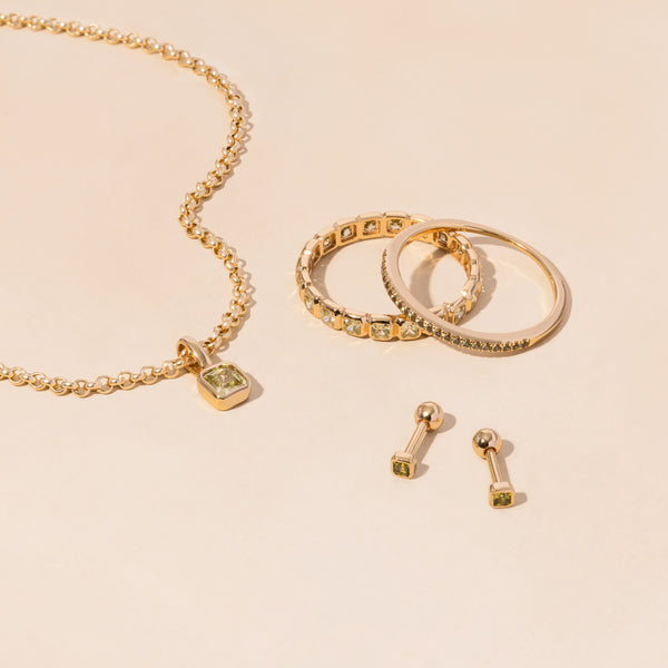 A gold necklace, rings, and earrings all adorned with light green gemstones.