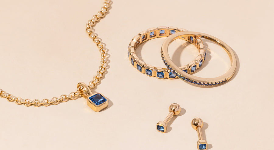 A gold necklace, rings, and earrings all adorned with blue gemstones.