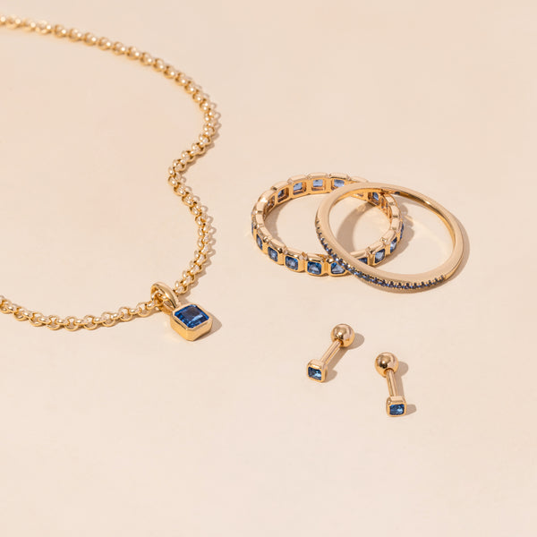 A gold necklace, rings, and earrings all adorned with blue gemstones.