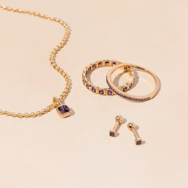 A gold necklace, rings, and earrings all adorned with purple gemstones.