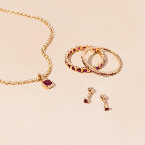 A gold necklace, rings, and earrings all adorned with dark red gemstones.