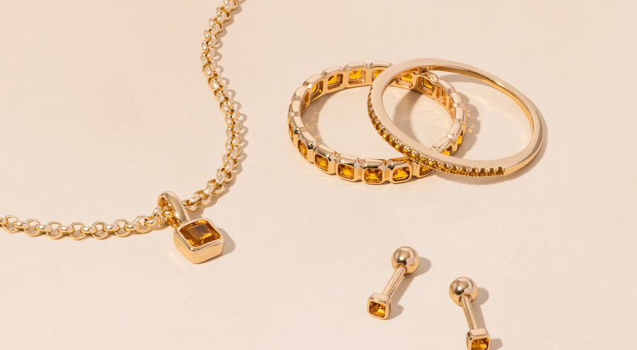 A gold necklace, rings, and earrings all adorned with amber colored gemstones.