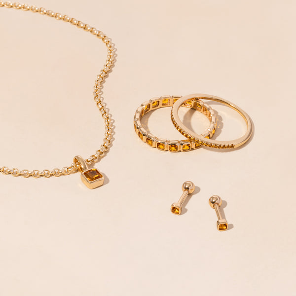 A gold necklace, rings, and earrings all adorned with amber colored gemstones.