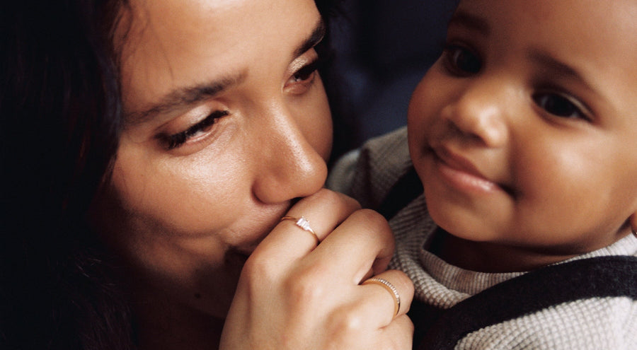 A woman holding her child and kissing his hand, showcasing multiple gold rings.