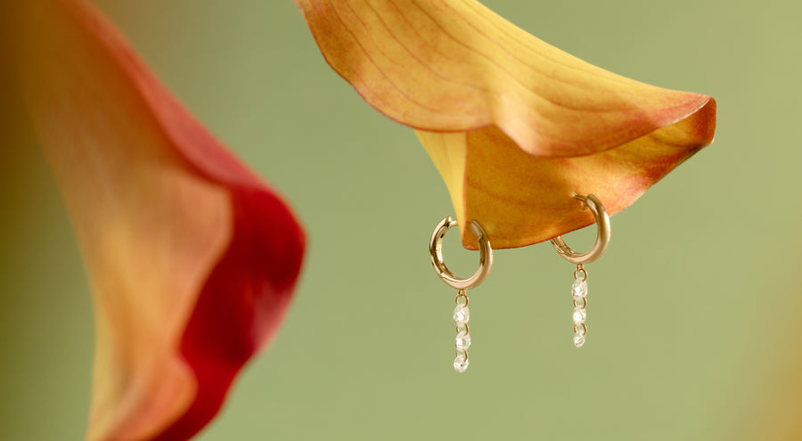 A yellow-orange orchid flower with two gold hoops hanging from it, with multiple clear crystals dangling down.