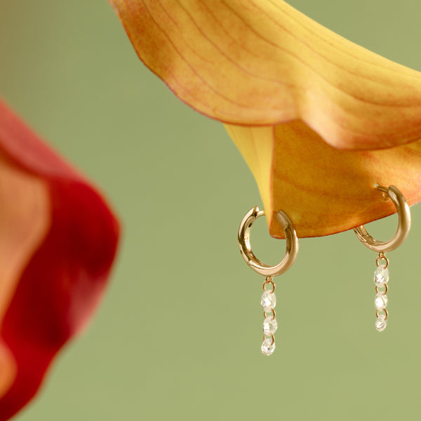 A yellow-orange orchid flower with two gold hoops hanging from it, with multiple clear crystals dangling down.