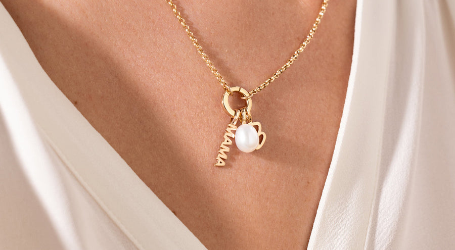 Gold necklace with a pearl charm, Script B Charm and 'MAMA' charm on a white shirt.