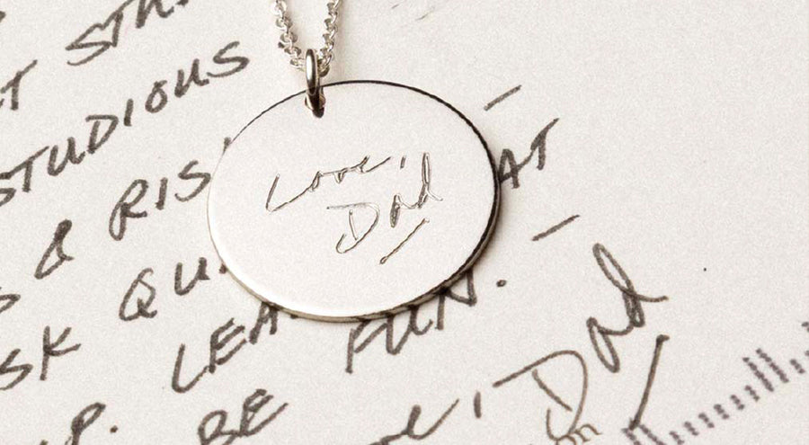 A silver round disc pendant necklace engraved with text, laying on a black and white handwritten letter.