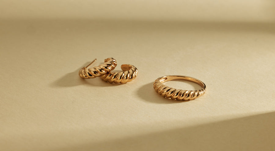 A pair of textured gold hoop earrings and a matching bold gold ring, laying on a light beige surface.
