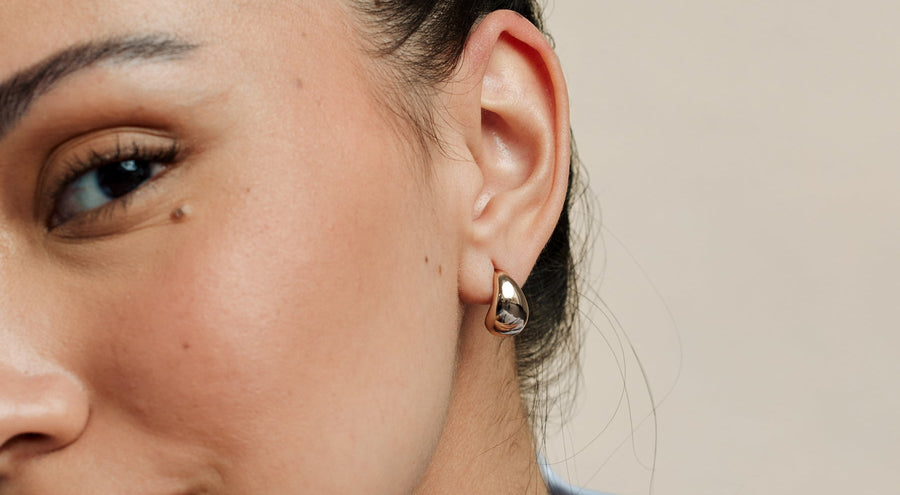 A person's ear wearing a single polished silver teardrop shaped stud earring.