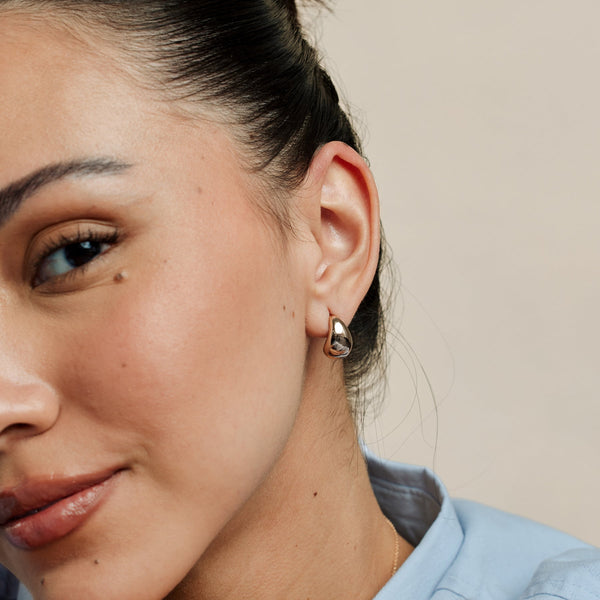 A person's ear wearing a single polished silver teardrop shaped stud earring.