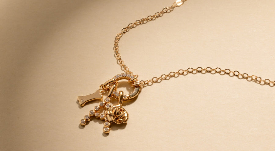 A gold chain charm necklace laying on a shadowy white surface, with multiple gold charms.
