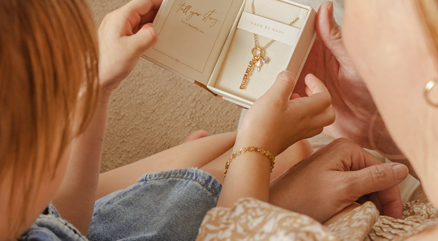 A child and grandmother holding an open jewelry box, showcasing a gold charm necklace.