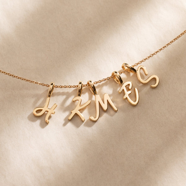 A gold pendant necklace with an initial H, K, M, E, and S charm in script font.