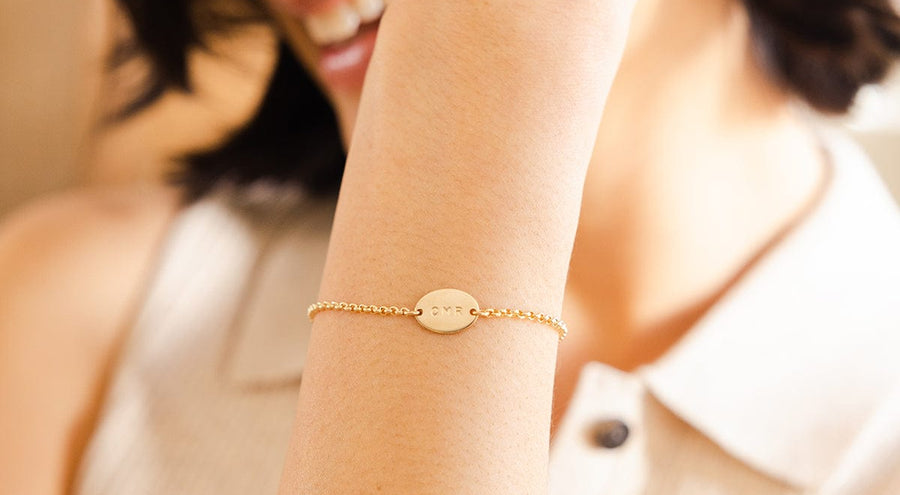 A person wearing a gold chain bracelet with an engraved oval in the center.