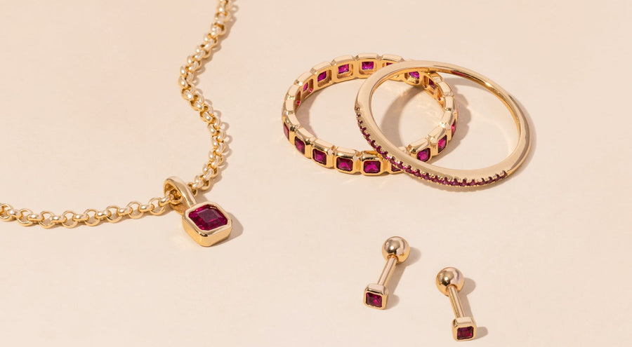 A gold necklace, rings, and earrings all adorned with dark red gemstones.