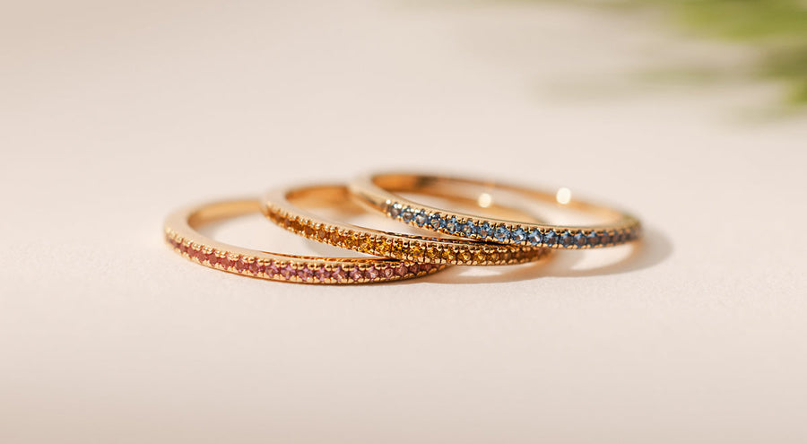 Three stacked thin gold rings, each with different colored gemstones.