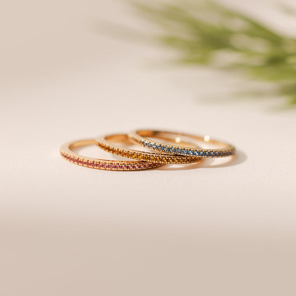 Three stacked thin gold rings, each with different colored gemstones.