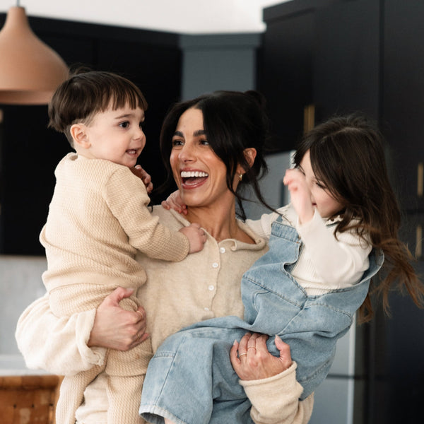 A mother holding her two children in a kitchen.