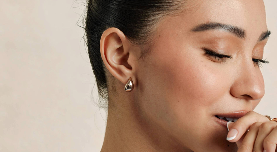 A close-up of a person's ear wearing a polished silver teardrop shaped stud earring.