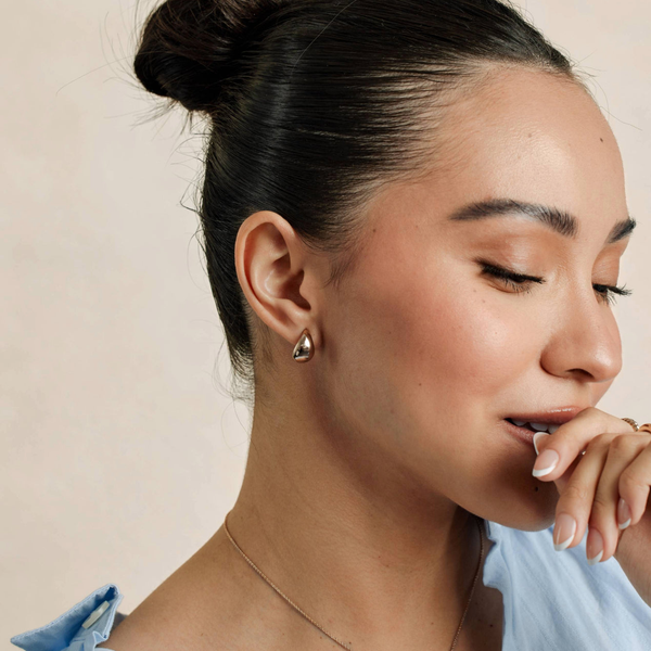 A close-up of a person's ear wearing a polished silver teardrop shaped stud earring.