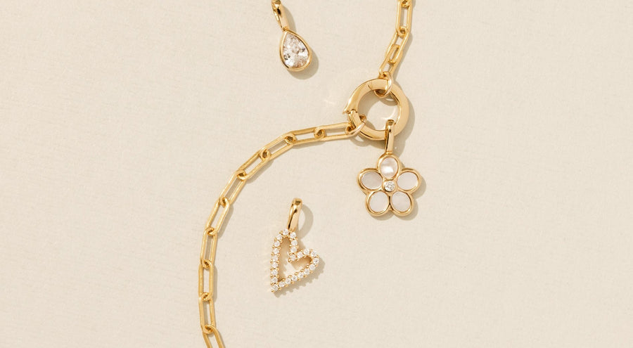 A gold paperclip chain charm bracelet with multiple gold charms, laying on a solid white surface.