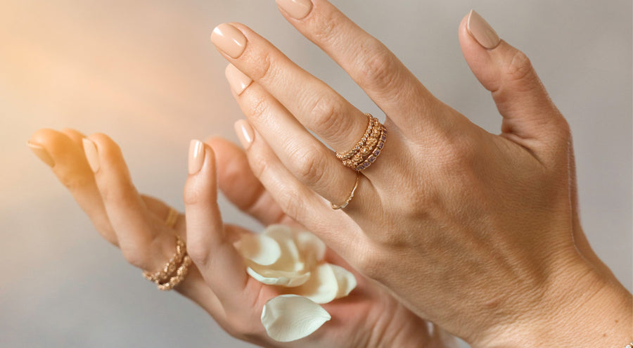Hands throwing white flower petals, wearing stacked gold rings in various styles.